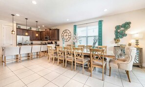 A spacious kitchen with modern appliances, a dining area with wooden chairs, and a decorative wall clock. - Charming Estate With Themed Bedrooms at Encore (Kissimmee)