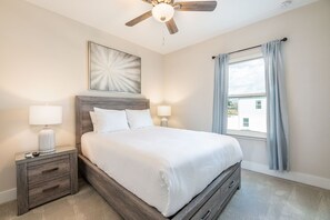 Ein Schlafzimmer mit Bett, Nachttischen, Deckenventilator, Fenster mit Vorhängen und einem Wandbild.
