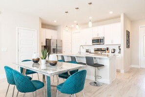 A modern kitchen with white cabinets, stainless steel appliances, and a central island with bar stools. - Aqua Townhouse With Games Room at Reunion (Kissimmee)