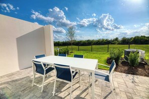 An outdoor patio with a white table and blue chairs, a black fence, and a grassy area with trees. - Aqua Townhouse With Games Room at Reunion (Kissimmee)