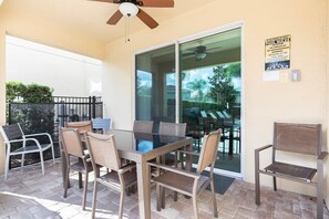 An outdoor patio with a glass table and chairs, a ceiling fan, and a pool rules sign. - 8BR Encore Villa Pool, Spa & Loft (Kissimmee)
