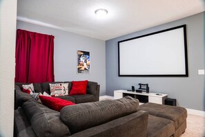 A home theater room with a large flat-screen TV, a sofa, and a coffee table. - 8BR Encore Villa Pool, Spa & Loft (Kissimmee)