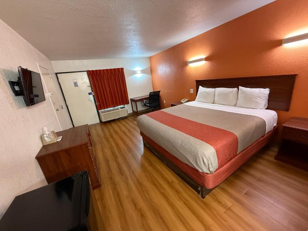 A hotel room with a bed, a desk, a chair, a mirror, and a door.