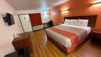 A hotel room with a bed, a desk, a chair, a mirror, and a door.