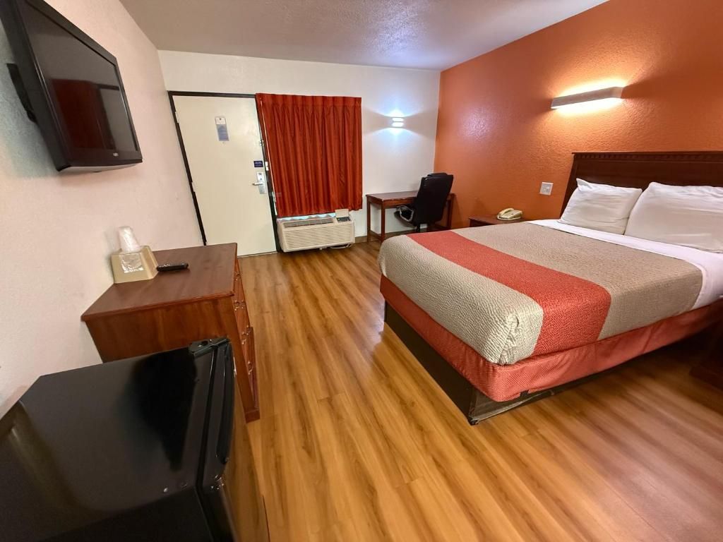 A hotel room with a bed, a desk with a chair, a television, and a door with a red curtain.