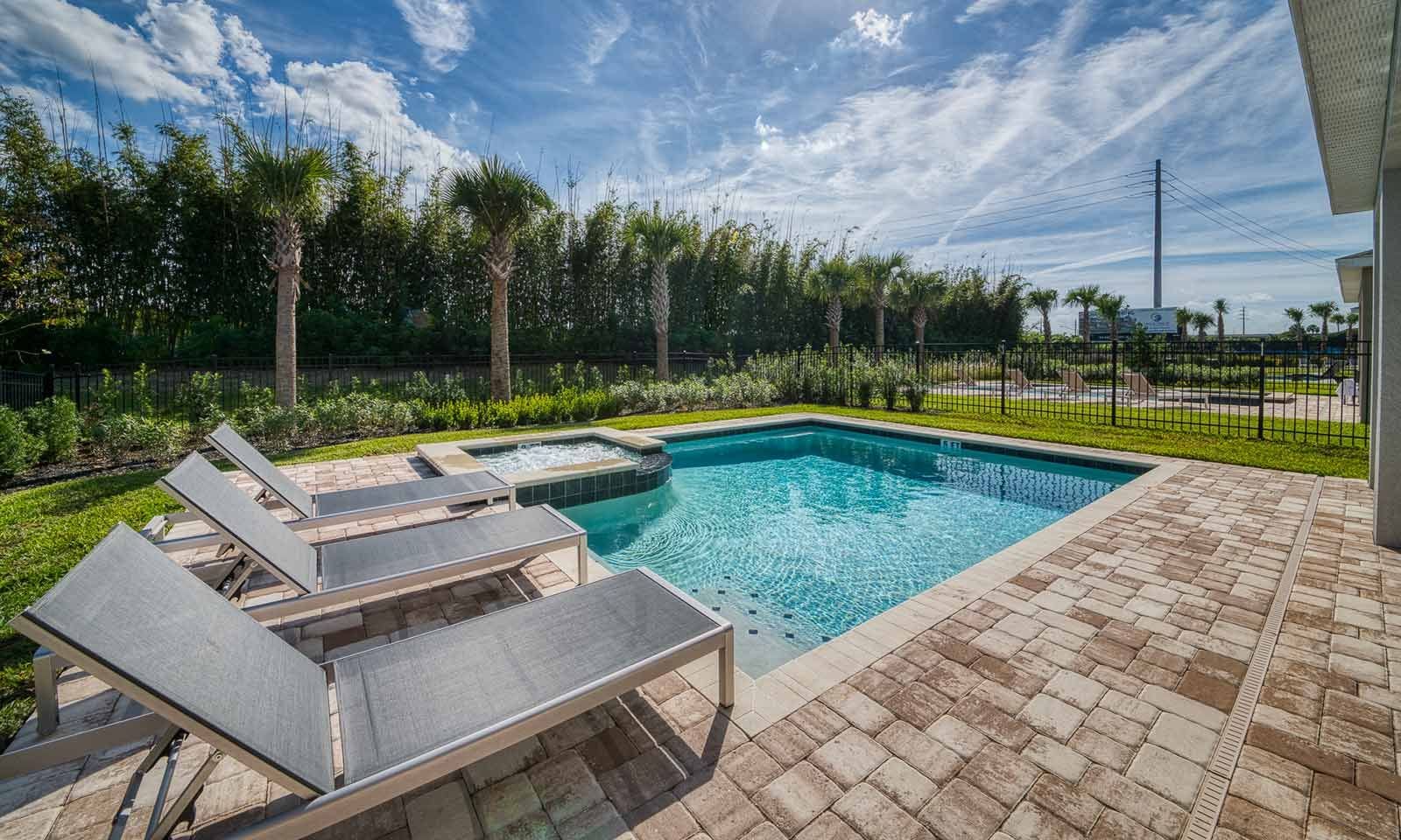 A rectangular swimming pool with a hot tub, surrounded by a brick patio and lounge chairs.