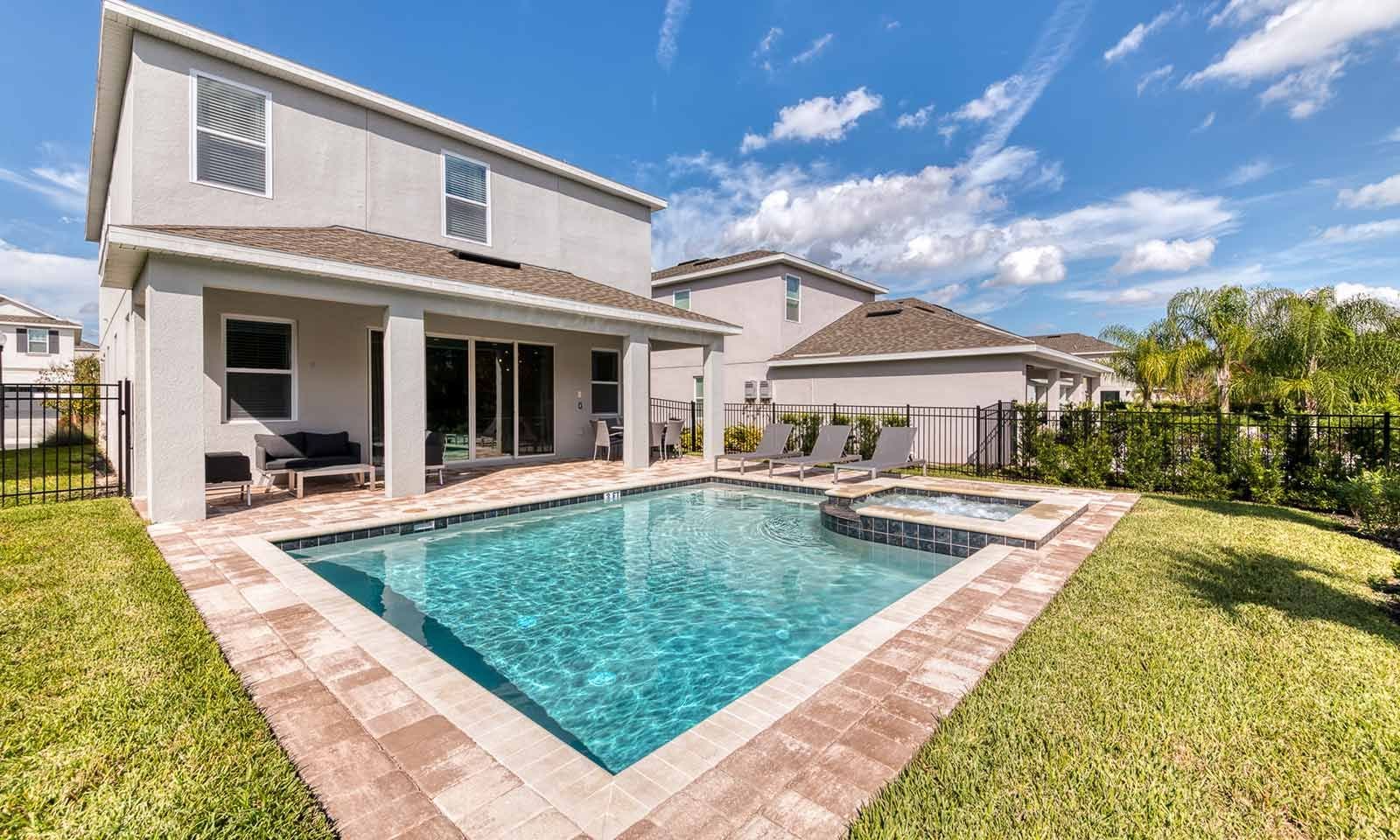 A two-story house with a swimming pool, a covered patio, and a fenced backyard.