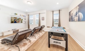 A modern room with a foosball table, reclining chairs, a TV, and a painting. - Classic Home With Private Pool at Encore (Kissimmee)
