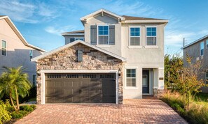 A two-story house with a stone facade, a garage, and a brick driveway. - Classic Home With Private Pool at Encore (Kissimmee)