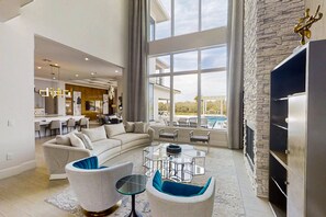 A spacious living room with a large window, a fireplace, and a modern kitchen in the background. - 6BR Reunion Mansion Circus Room & Karaoke (Kissimmee)