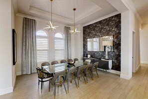A modern dining area with a glass table, grey chairs, and a stone accent wall. - 6BR Reunion Mansion Circus Room & Karaoke (Kissimmee)