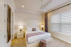 Een hotelkamer met een groot bed, twee nachtkastjes met lampen, een plafondventilator en een raam met jaloezieën.