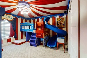 Een speelkamer met een circusthema, met een glijbaan, een trein en een bord waarop staat 'Circus'.
