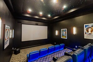 A movie theater with blue seating, a large screen, and posters on the walls. - 6BR Reunion Mansion Circus Room & Karaoke (Kissimmee)