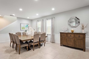 A dining area with a wooden table and chairs, a cabinet, and a staircase. - Encore 7BR Villa, Pool, Near Disney (Kissimmee)