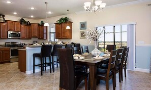 A modern kitchen with wooden cabinets, stainless steel appliances, and a dining area with a large island and chairs. - 6BR Championsgate Villa Pool, Spa & Game Room (Davenport)