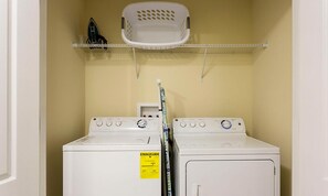 A laundry room with two white washers and dryers, a white basket on a shelf, and a yellow energy guide sticker on the dryer. - 8BR Championsgate Villa Pool, Spa & Theater (Davenport)