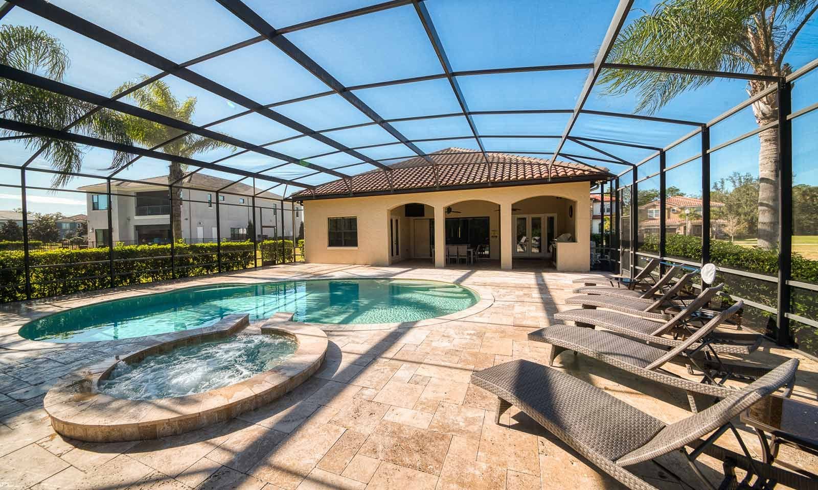 A covered outdoor swimming pool with lounge chairs, a hot tub, and a building with a tiled roof.