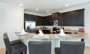 A modern kitchen with dark cabinets, granite countertops, stainless steel appliances, and a bar area with seating. - 5BR Encore Villa With Private Pool & Spa (Kissimmee)