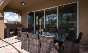 An outdoor patio with wicker furniture and a glass door leading to a pool area. - 5BR Encore Villa With Private Pool & Spa (Kissimmee)