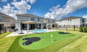 Ein Wohnhaus mit Swimmingpool, einer Terrasse mit Liegestühlen und einem gepflegten Rasen.
