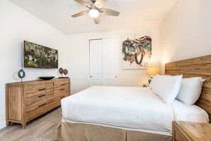 A bedroom with a bed, wooden dresser, ceiling fan, artwork, and a door. - Encore 8BR Home, Pool & Spa, 10 Min to Disney (Kissimmee)