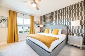 Un dormitorio moderno con una cama grande, un ventilador de techo, una mesita de noche con lámpara y un papel tapiz estampado.