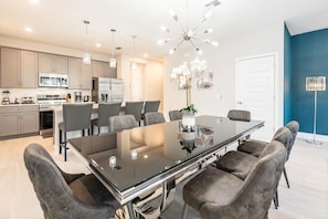 Cocina moderna con comedor, que incluye una mesa de vidrio, sillas tapizadas en gris e iluminación colgante.