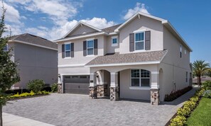 A two-story house with a garage, stone pillars, and a paved driveway. - Encore 8BR Villa, Putting Green, Near Disney (Kissimmee)