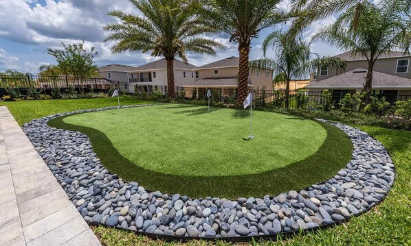 A well-maintained lawn with a circular stone border, palm trees, and a row of houses in the background. - Encore 8BR Villa, Putting Green, Near Disney (Kissimmee)