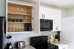 Una cucina con mobili bianchi, un forno a microonde nero, un tostapane e un frullatore.