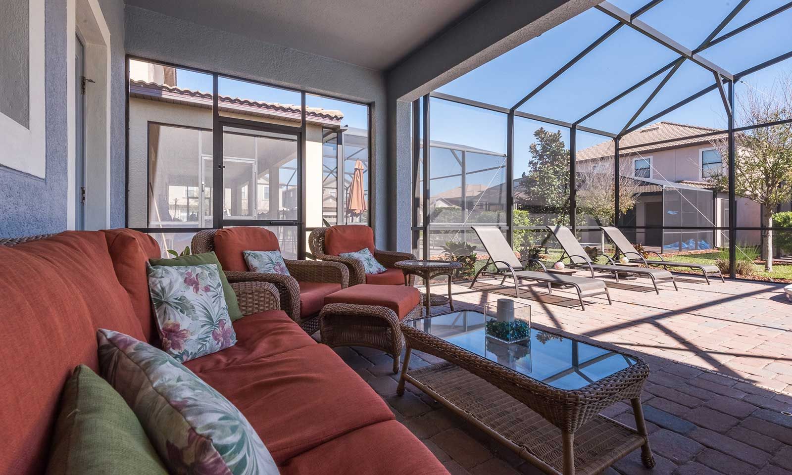Une terrasse couverte, aménagée avec des meubles en osier, une table en verre et offrant une vue sur le quartier.
