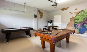 Ein Billardtisch, eine Wand mit Spinnweben-Design, ein an der Decke montierter Projektor und ein Wandgemälde einer grünen Figur.
