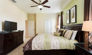 A bedroom with a bed, dresser, television, ceiling fan, and artwork on the walls. - 8BR Championsgate Villa Pool, Spa & Theater (Davenport)