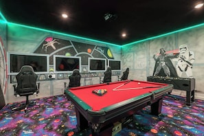 Ein Billardtisch in einem Raum mit mehreren Bildschirmen, einem Gaming-Sessel und einem Wandgemälde zum Thema Star Wars.