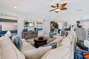 A spacious living room with a large sofa set, a coffee table, and a ceiling fan. - 8BR Vacation Home With Screened Pool Area (Kissimmee)