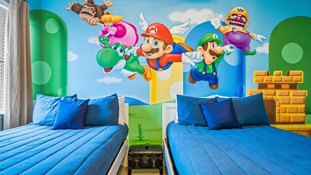 A room with two beds, a mural of video game characters, and a brick wall design. - 8BR Vacation Home With Screened Pool Area (Kissimmee)