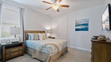 A bedroom with a bed, nightstands, a ceiling fan, a window with blinds, a door, and a wall-mounted TV.