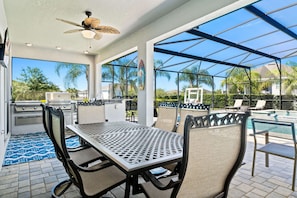 An outdoor patio with a grill, seating, and a pool area. - 8BR Vacation Home With Screened Pool Area (Kissimmee)