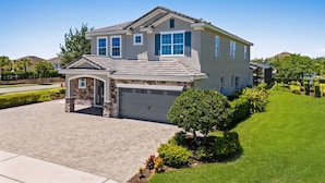 A two-story house with a garage, a driveway, and a well-maintained lawn. - 8BR Vacation Home With Screened Pool Area (Kissimmee)