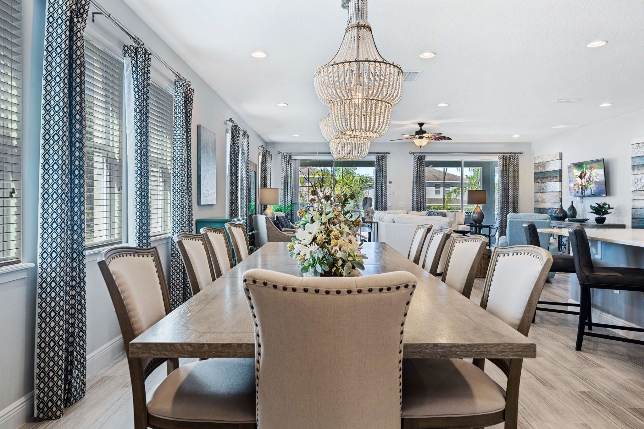 A dining area with a long table, chairs, a chandelier, and a view of the outdoors.