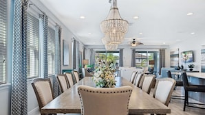 A dining area with a long table, chairs, a chandelier, and a view of the outdoors. - 8BR Vacation Home With Screened Pool Area (Kissimmee)