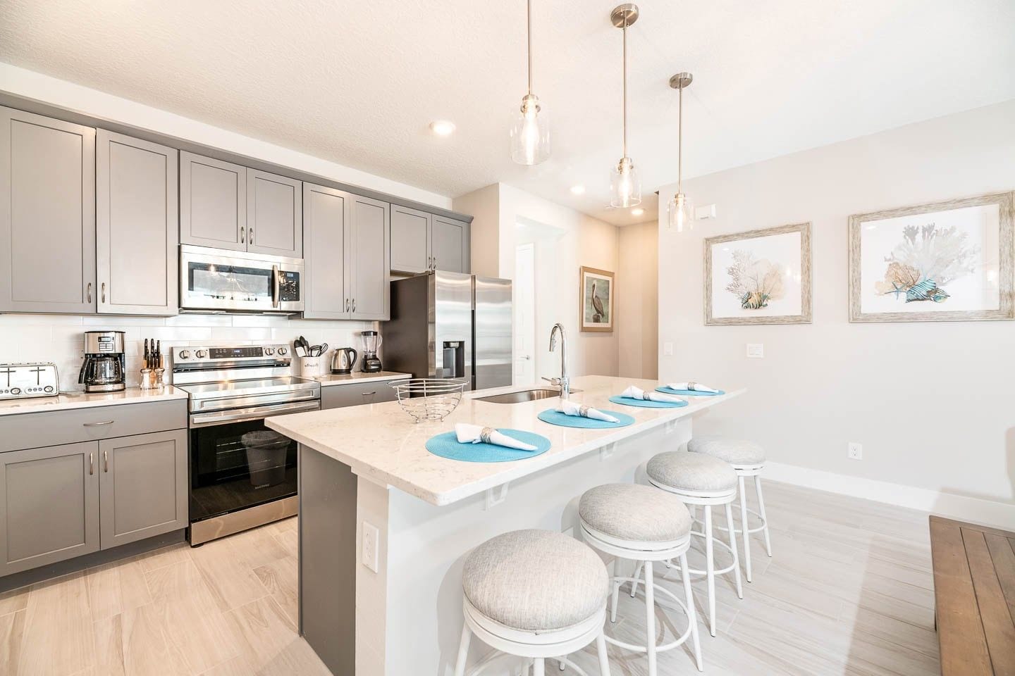 A modern kitchen with grey cabinets, stainless steel appliances, a central island with stools, and pendant lighting.