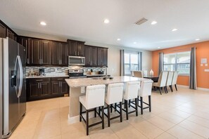 A modern kitchen with dark wood cabinets, a stainless steel refrigerator, a microwave, and a large island with bar stools. - Encore 8BR Villa, Home Theater, Near Disney (Kissimmee)