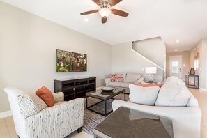 A living room with a sofa, armchair, coffee table, TV, and a staircase leading to another room. - Encore 8BR Villa, Home Theater, Near Disney (Kissimmee)