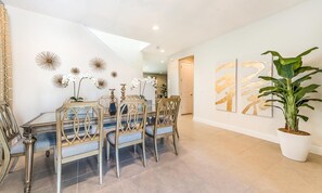 A dining area with a glass table, wooden chairs, and decorative wall art. - Delightful Home With Private Pool Oasis in Encore (Kissimmee)