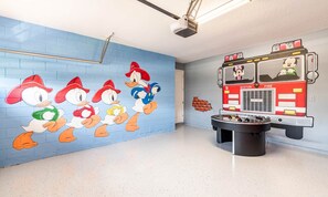 A room with a blue brick wall mural of cartoon ducks, a fire truck mural, and a foosball table. - Delightful Home With Private Pool Oasis in Encore (Kissimmee)
