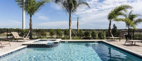 A rectangular swimming pool with a hot tub, surrounded by lounge chairs and palm trees.