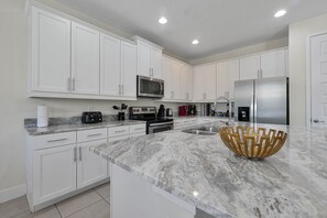 A modern kitchen with white cabinets, a stainless steel refrigerator, a microwave, and a marble countertop. - Encore Resort 5BR Home With Game Room (Kissimmee)