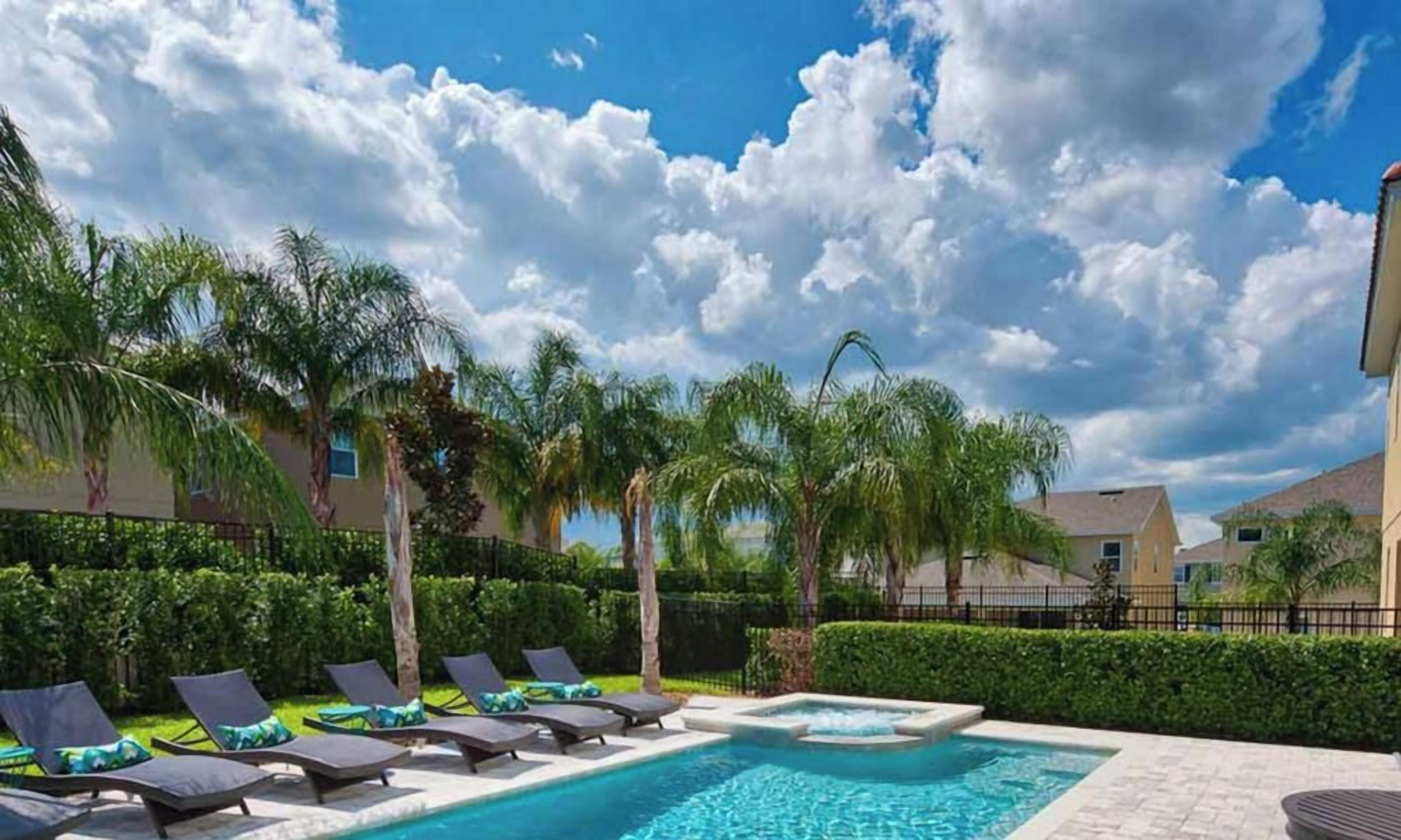 A swimming pool with lounge chairs, palm trees, and a clear sky.
